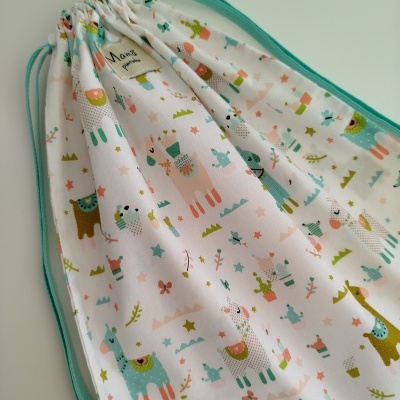 Saco de tecido branco com padrão de lhamas e cordões verdes.