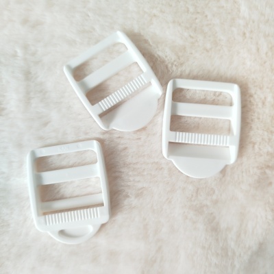 Três fivelas reguladoras plásticas brancas sobre superfície felpuda