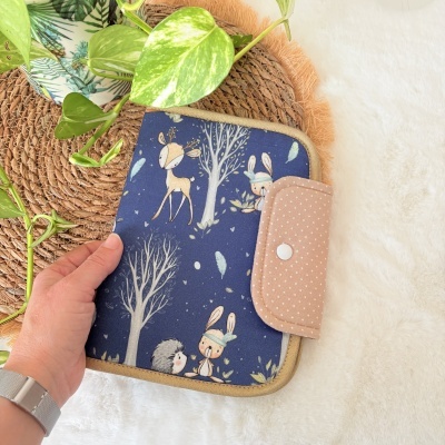 Capa em tecido azul com ilustração de animais e árvores, fecho de aba rosa com bolas brancas.