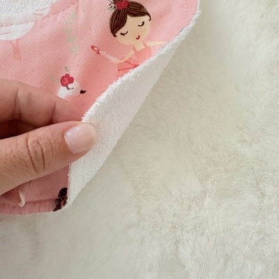 Babete de bebé rosa com padrão de bailarinas e cisnes, reverso branco felpudo