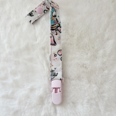 Tira para chupeta com tecido estampado e fecho lilás sobre fundo branco felpudo