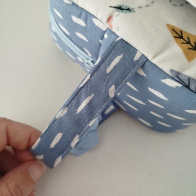 Fecho em tecido azul com padrão branco e parte de almofada ou brinquedo macio com desenhos de folhas