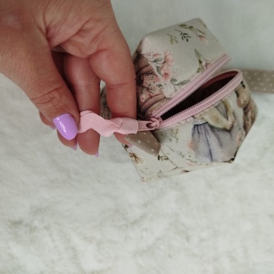 Bolsa pequena em tecido floral com zipper rosa segurada por mão com unhas lilás