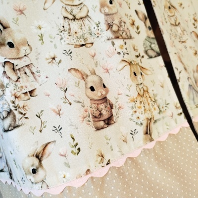Tecido com estampa de coelhinhos e flores em tons suaves, com fita rosa ondulada e fundo bege com bolinhas brancas