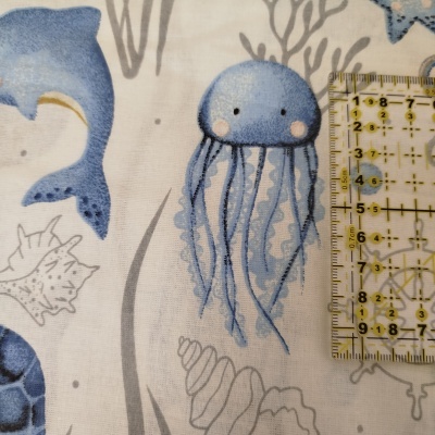 Tecido branco com estampado de animais marinhos em azul e cinza com régua amarela para escala
