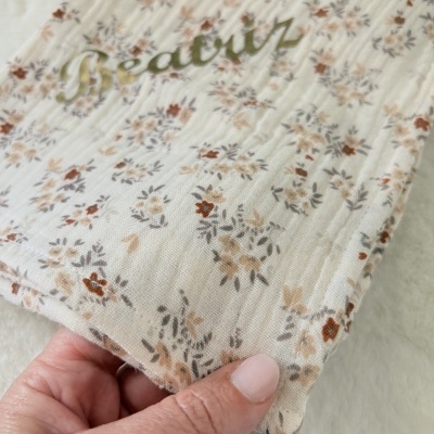 Tecido branco com padrão floral castanho e cinza e texto verde Beatruz