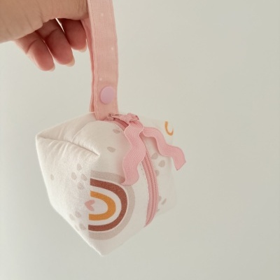 Bolsa pequena branca com padrão colorido e fecho rosa sendo segurada por uma mão