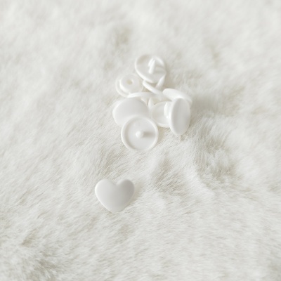 Botões de pressão brancos redondos e em forma de coração sobre superfície branca felpuda.