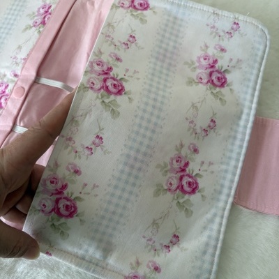 Organizador de tecido com padrão floral cor-de-rosa e riscas azuis, interior rosa, fecho e elásticos brancos.