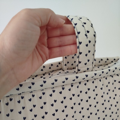 Bolsa de tecido bege com corações preto e alça acolchoada segurada por mão