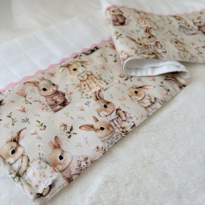Fralda de tecido branco com padrão de coelhos e acabamento rosa