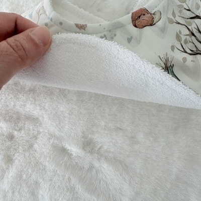 Manta ou fralda branca felpuda com tecido estampado com árvores coloridas e mão segurando canto.