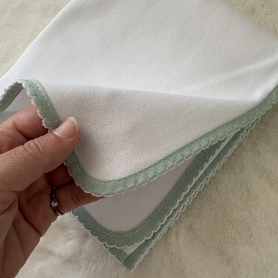 Guardanapo branco com borda verde segurado por uma mão sobre superfície macia