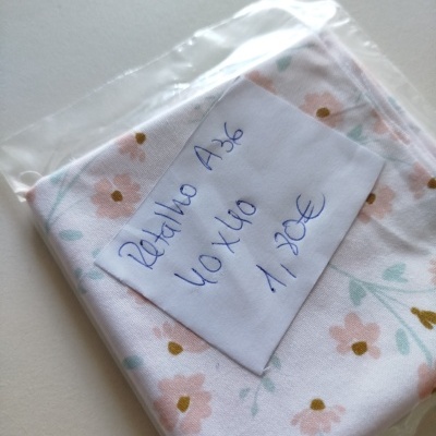 Retalho de tecido branco com padrão floral em tons de rosa, verde e amarelo num saco plástico com etiqueta manuscrita