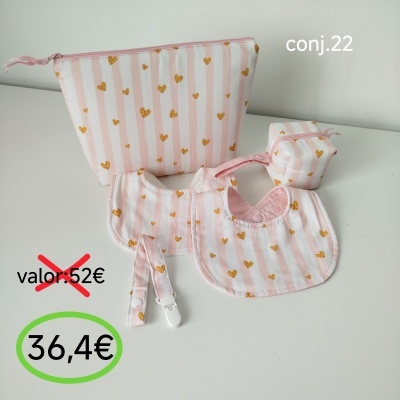 Conjunto de artigos em tecido rosa com corações dourados e riscas, babetes, presilha e necessaires sobre mesa branca