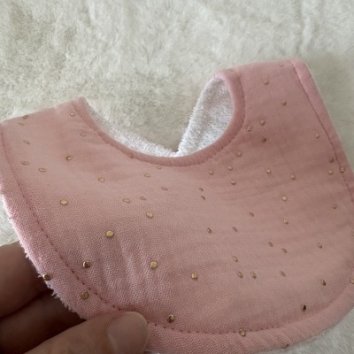 Babete para bebé rosa com pontos dourados e interior branco, segurado por uma mão