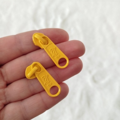 Dois puxadores de fecho éclair amarelos em plástico com a palavra cope em relevo na mão