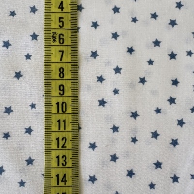 Tecido branco com estrelas azuis e régua de tapeçaria amarela com marcações de centímetros
