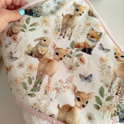 Toalha de bebê com estampa de animais e flores em tons pastel com borda rosa às riscas