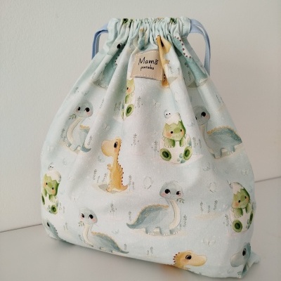 Saco de tecido azul claro com estampado de dinossauros e etiqueta 'Mama pintinhos'