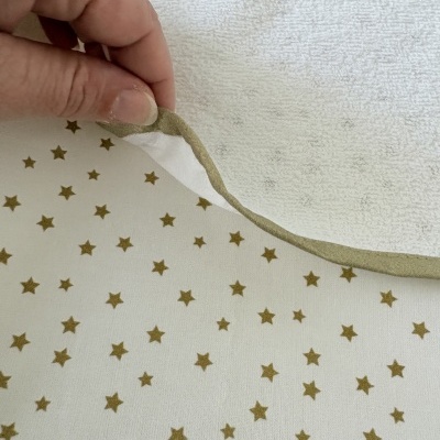 Tecido branco felpudo com borda verde segurado por mão sobre tecido branco com estrelas douradas