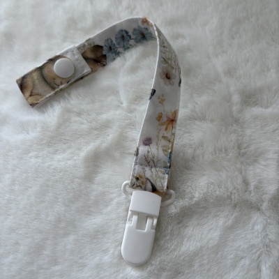 Prendedor branco com fita de tecido floral sobre superfície branca macia