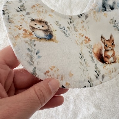 Babete de tecido branco com desenhos de ouriço e esquilo em tons castanhos e azul