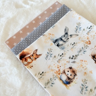 Tecidos dobrados com padrões de animais e formas geométricas sobre fundo branco peludo