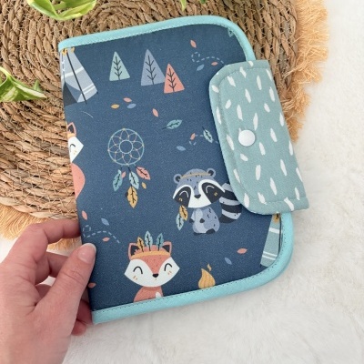 Estojo azul com desenhos infantis e fecho de pressão sobre superfície branca e ráfia