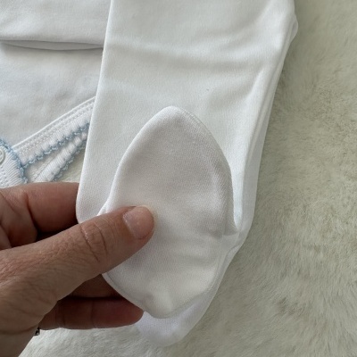 Peça de tecido branco com detalhe de pé mostrado numa mão sobre fundo felpudo branco.