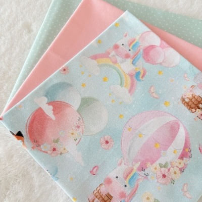 Tecidos dobrados com padrão de unicórnios e bolinhas, cores azul, rosa e verde claro