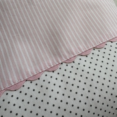 Guardanapo cor-de-rosa às riscas com borda ondulada sobre tecido branco com bolinhas pretas