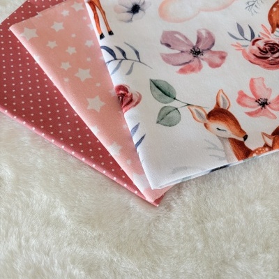 tecidos dobrados com padrões de poás, estrelas e veados sobre superfície branca felpuda