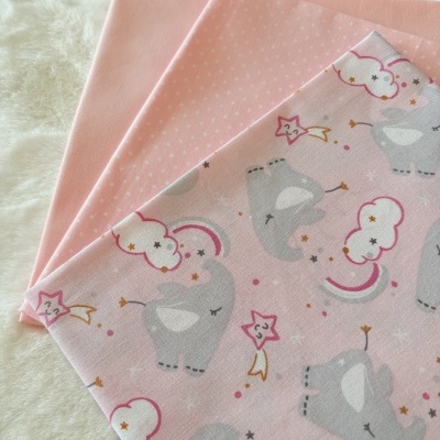 três tecidos rosa com padrão de elefantes e pontos sobre superfície branca felpuda