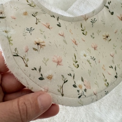 Babete com padrão floral tons pastel fundo bege e interior branco felpudo.