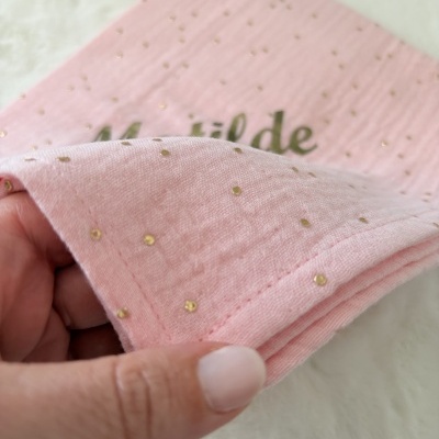 Pano de tecido rosa com pontos dourados e textura suave segurado por uma mão