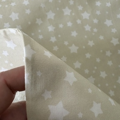 Tecido bege com estampado de estrelas brancas sendo segurado por uma mão.