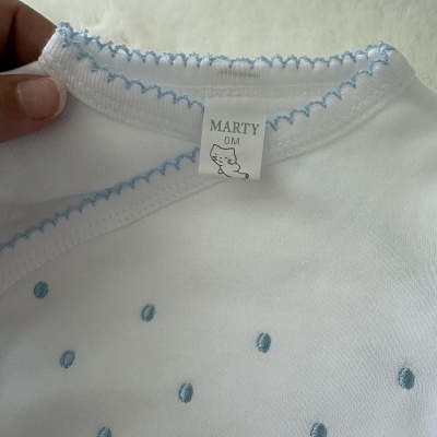Roupa de bebé branca com bordados azuis e etiqueta com gato MARTY OM