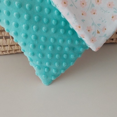 Manta dupla face azul turquesa com pontos salientes e branco com padrão floral em cesta de palha
