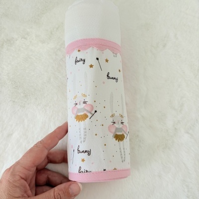 Fralda ou toalha de bebé branca e estampada com coelhinhos, estrelas e texto, fundo branco felpudo