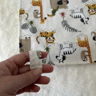 Tecido branco com estampado colorido de animais da selva e mão segurando uma tira do tecido