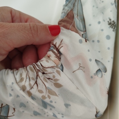 Tecido elástico com padrão natural e borboletas segurado por mão com unhas vermelhas