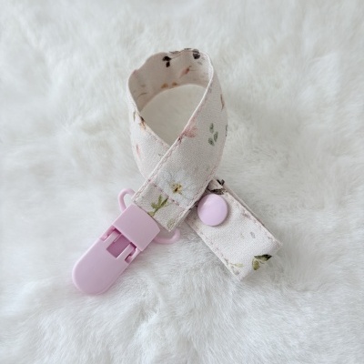 Clip chupeta floral com presilha rosa sobre fundo branco felpudo