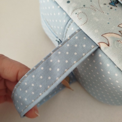 Alça de tecido azul com bolinhas brancas sendo segurada por mão junto de mala azul com bolinhas brancas