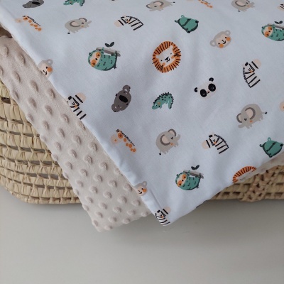 Manta dupla face com padrões de animais e textura em relevo sobre cesto de vime