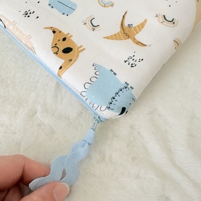 Bolsa de tecido com padrão de dinossauros coloridos e fecho azul claro.
