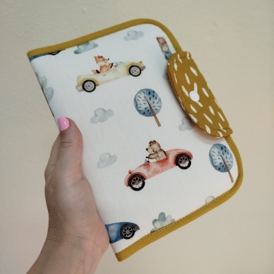 Capa com padrão de carros, animais e árvores, bordas amarelas e fecho, em tecido.