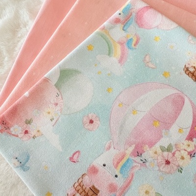 Panos de tecido rosa e estampado com unicórnios e balões sobre superfície de peluche.