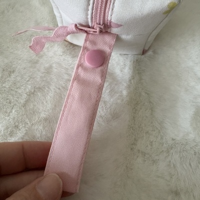 Bolsa de tecido branco com fecho de correr cor de rosa e alça rosa com botão de pressão.