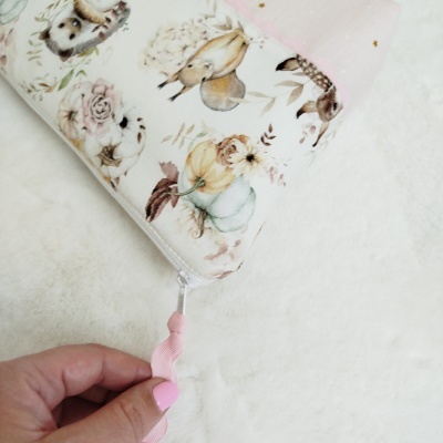 Estojo com padrão de animais e flores em tons suaves e fecho com puxador rosa.